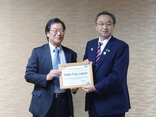 イクレイの竹本理事長と佐渡市長が会員証を掲げている写真です。
